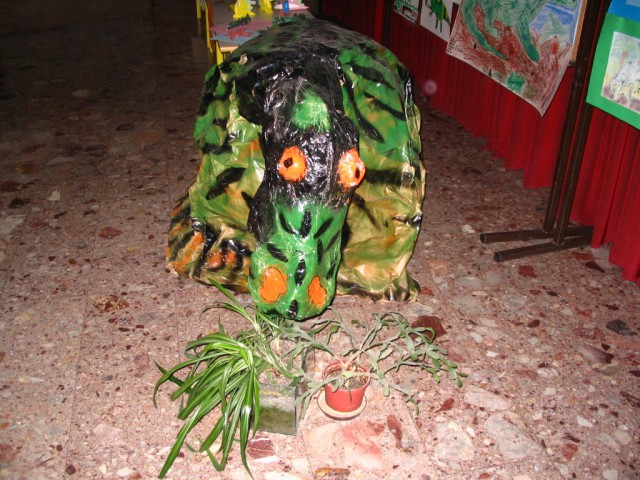 Kaširan dinozaver in posprejan z oranžnim, zelenim in črnim sprejem.